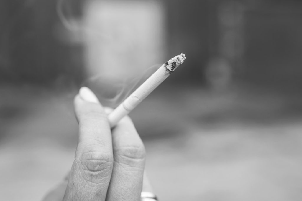 Une main tient une cigarette, sur une photographie en noir et blanc.